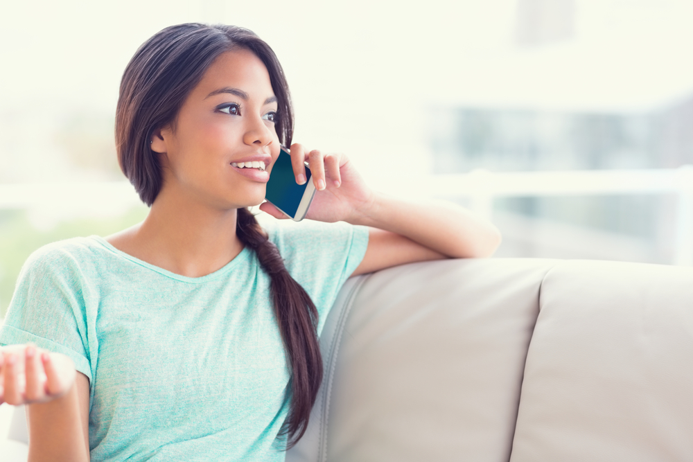 Cheerful girl sitting on sofa making a phone call at home in the living room